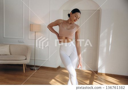 Creamy colored top and white pants. Young woman in fitness clothes is in the room Creamy colored top and white pants. Young woman in fitness clothes is in the room 136761382