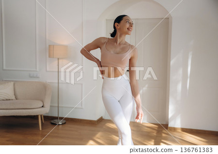 Creamy colored top and white pants. Young woman in fitness clothes is in the room Creamy colored top and white pants. Young woman in fitness clothes is in the room 136761383