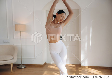 Creamy colored top and white pants. Young woman in fitness clothes is in the room Creamy colored top and white pants. Young woman in fitness clothes is in the room 136761384