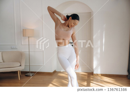 Creamy colored top and white pants. Young woman in fitness clothes is in the room 136761386