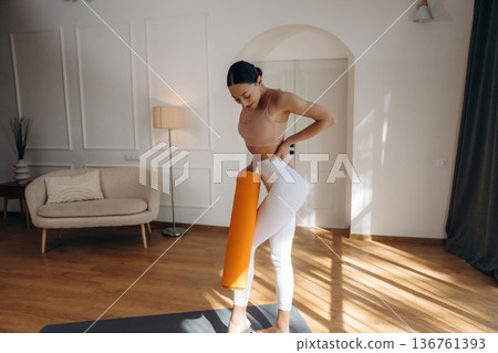 The orange fitness roll. Young woman in fitness clothes is in the room The orange fitness roll. Young woman in fitness clothes is in the room 136761393