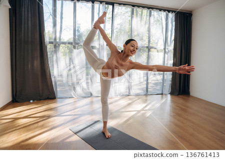 One leg is up, standing. Young woman in fitness clothes is in the room 136761413
