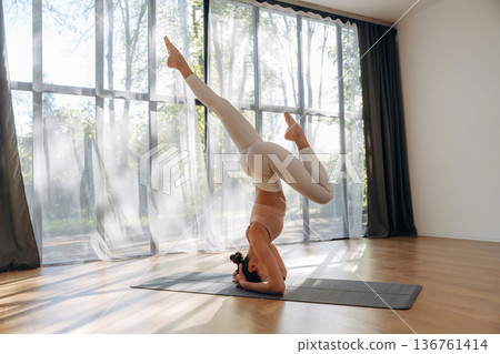 Strength to do headstand. Young woman in fitness clothes is in the room Strength to do headstand. Young woman in fitness clothes is in the room 136761414