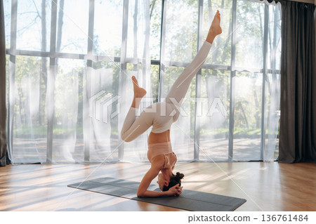 Daylight is going through the panoramic window. Young woman in fitness clothes is in the room 136761484