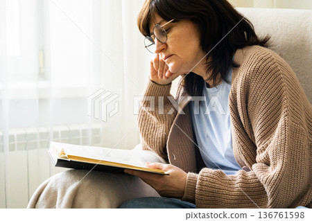 Woman wearing glasses reading book at home 136761598