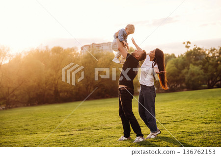 Holding kid in hands. Family of mother, father and son are playing on the field Holding kid in hands. Family of mother, father and son are playing on the field 136762153