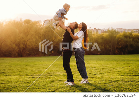 Holding kid in hands. Family of mother, father and son are playing on the field Holding kid in hands. Family of mother, father and son are playing on the field 136762154