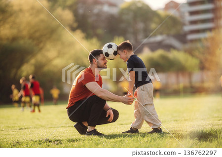 Keeping soccer ball by heads. Father and son are having fun outdoors 136762297