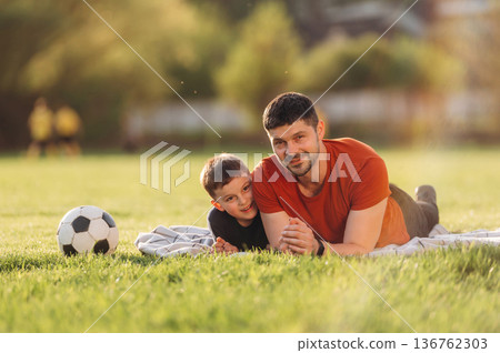 Front view, lying down. Father and son are having fun outdoors Front view, lying down. Father and son are having fun outdoors 136762303