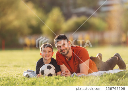 Front view, lying down. Father and son are having fun outdoors Front view, lying down. Father and son are having fun outdoors 136762306