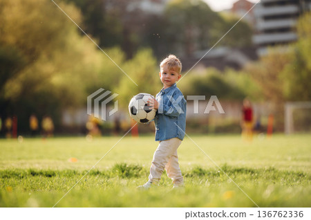 In blue shirt, with soccer ball. Little boy is having fun on the field outdoors 136762336