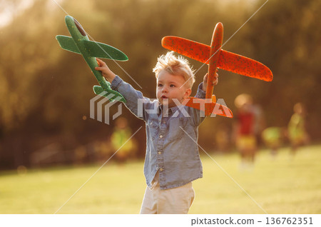 Two toy planes are in hands. Little boy is having fun on the field outdoors 136762351