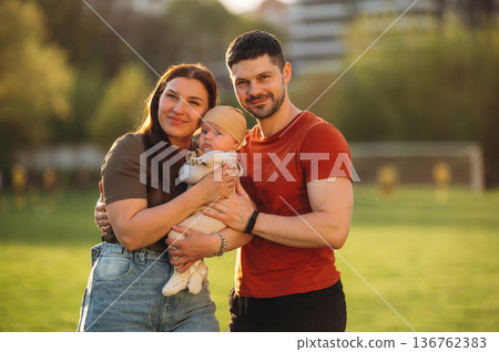 Positive facial expression. Happy couple parents are with little baby outdoors Positive facial expression. Happy couple parents are with little baby outdoors 136762383