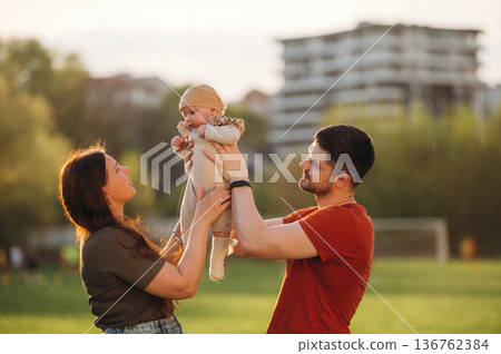 Positive facial expression. Happy couple parents are with little baby outdoors Positive facial expression. Happy couple parents are with little baby outdoors 136762384