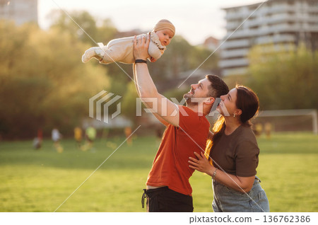 Positive facial expression. Happy couple parents are with little baby outdoors Positive facial expression. Happy couple parents are with little baby outdoors 136762386