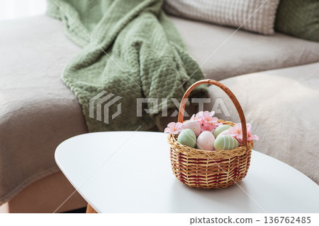 Easter Basket with Ester Eggs,  Plush Bunny and Spring Decor on White Table intoCozy Living Room 136762485