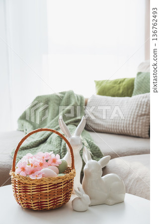 Easter Basket with Ester Eggs,  Plush Bunny and Spring Decor on White Table intoCozy Living Room 136762493