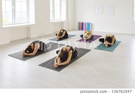 Yoga class in forward fold, group on mats in bright studio environment together 136762847