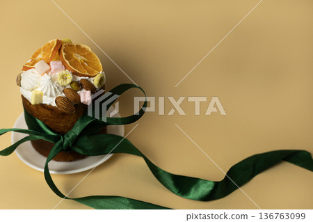 Traditional Easter cake decorated with almonds, marshmallows and orange slices served on white plate with dark green satin ribbon Traditional Easter cake decorated with almonds, marshmallows and orange slices served on white plate with dark green satin ribbon 136763099