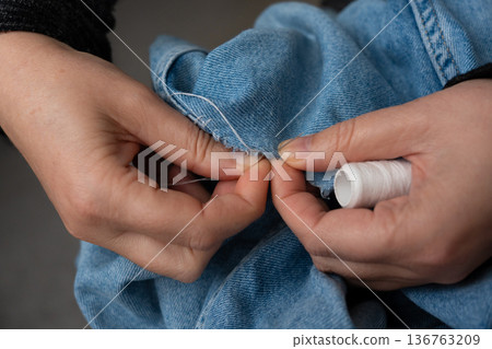 Woman mends jeans by hand with needle 136763209