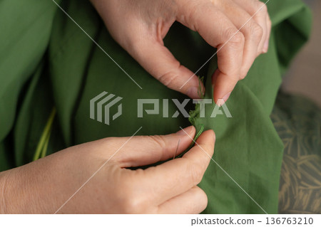 Woman darning a green jacket by hand with needle and patch fabric Woman darning a green jacket by hand with needle and patch fabric 136763210