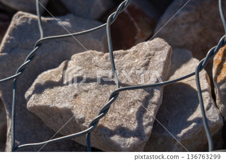 Gabion stone wall construction close up. New stone fence in wire grid, iron cage with rocks Gabion stone wall construction close up. New stone fence in wire grid, iron cage with rocks 136763299