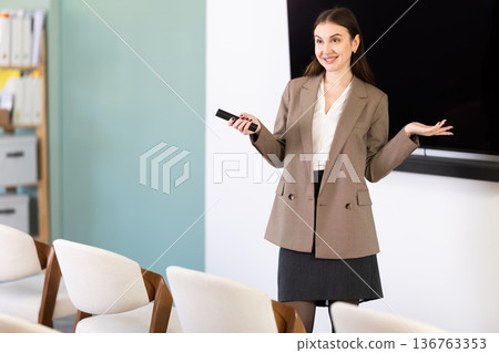 Young woman coach presenting in auditorium with remote control Young woman coach presenting in auditorium with remote control 136763353