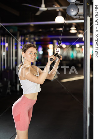Slender athletic woman work out muscles of hands on cable crossover machine in fitness club 136763494