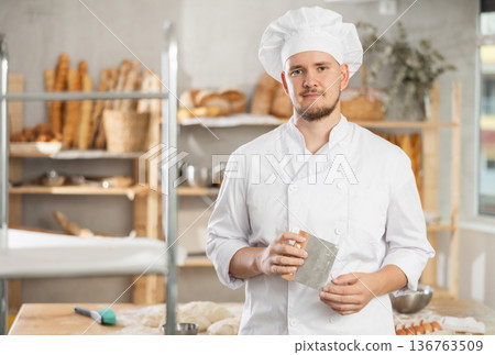 Male baker stands near work table in bakery, resting while working. 136763509