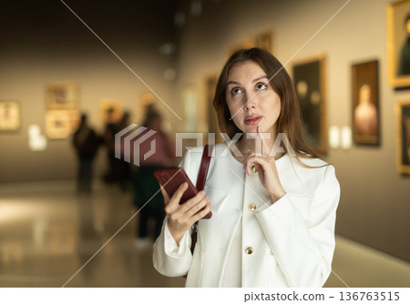 Woman with mobile phone on the background of paintings 136763515