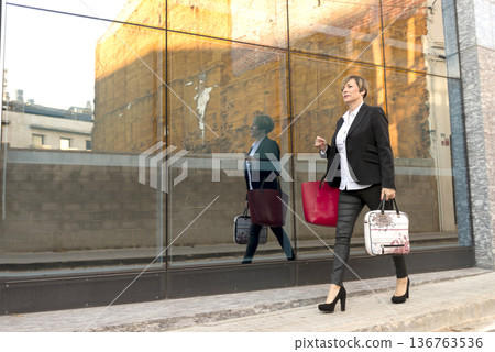Businesswoman walking by glass wall with reflection 136763536