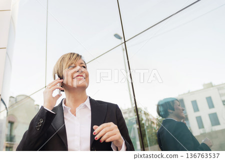 Businesswoman on phone by modern glass building Businesswoman on phone by modern glass building 136763537