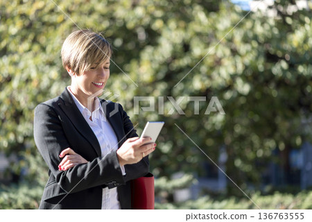 Businesswoman using smartphone outdoors in park Businesswoman using smartphone outdoors in park 136763555