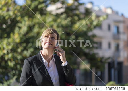 Businesswoman talking on phone outdoors in city 136763556