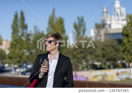 Businesswoman with coffee standing in city park 136763565