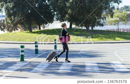 Businesswoman crossing street with suitcase 136763578
