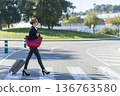 Businesswoman crossing street with suitcase 136763580