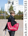 Businesswoman with red bag walking in city 136763583