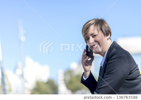 Businesswoman smiling while talking on smartphone Businesswoman smiling while talking on smartphone 136763586