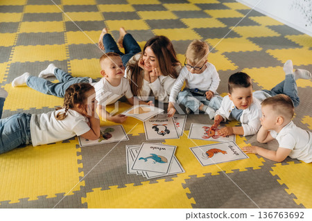 Lying down on floor, learning new words. Children in kindergarten with their teacher Lying down on floor, learning new words. Children in kindergarten with their teacher 136763692