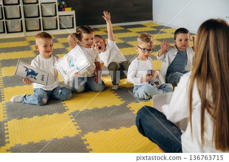 Thinking, learning, sitting on the table. Children in kindergarten with their teacher Thinking, learning, sitting on the table. Children in kindergarten with their teacher 136763715
