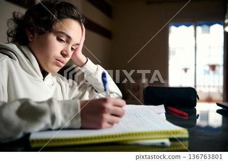 Teenage Boy Studying Homework at Night in Cozy Home Interior Focused and Thoughtful Teenage Boy Studying Homework at Night in Cozy Home Interior Focused and Thoughtful 136763801