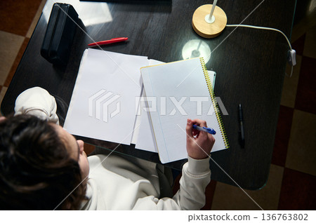 Teenage Boy Doing Homework At A Cozy Home Desk In The Evening Light Teenage Boy Doing Homework At A Cozy Home Desk In The Evening Light 136763802