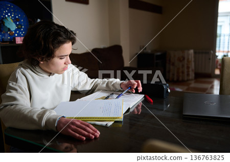 Teenage Boy Doing Homework In The Evening At A Cozy Home Interior Teenage Boy Doing Homework In The Evening At A Cozy Home Interior 136763825