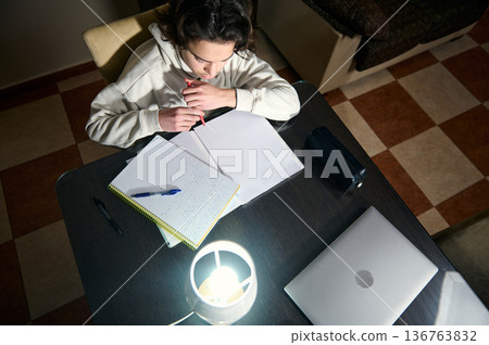 Teenage Boy Doing Homework At A Cozy Home Desk Under Warm Lamp Light In The Evening Teenage Boy Doing Homework At A Cozy Home Desk Under Warm Lamp Light In The Evening 136763832