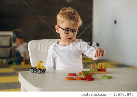 White shirt, eyewear, sitting by table and playing. Group of children are in the kindergarten 136763845