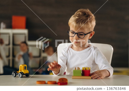 White shirt, eyewear, sitting by table and playing. Group of children are in the kindergarten 136763846