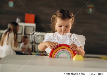 Girl is sitting and playing with toy. Group of children are in the kindergarten 136763896