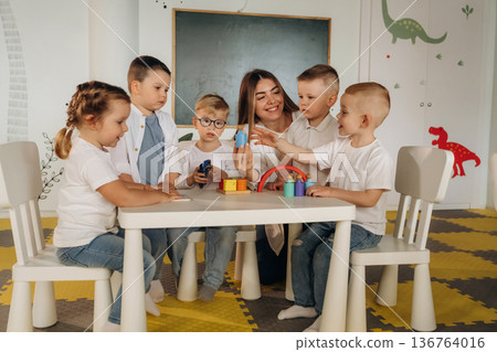 Sitting by the table. Children in kindergarten with their teacher 136764016