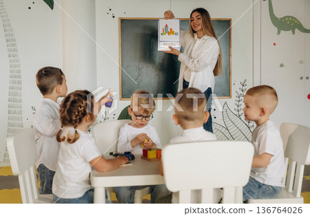 Woman is showing picture of object. Children in kindergarten with their teacher Woman is showing picture of object. Children in kindergarten with their teacher 136764026